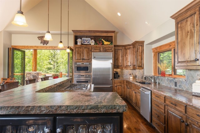 460 Two Cabins Dr, Silverthorne, CO 80498 - kitchen with appliances with stainless steel finishes, dark countertops, brown cabinetry, a kitchen island, and high vaulted ceiling