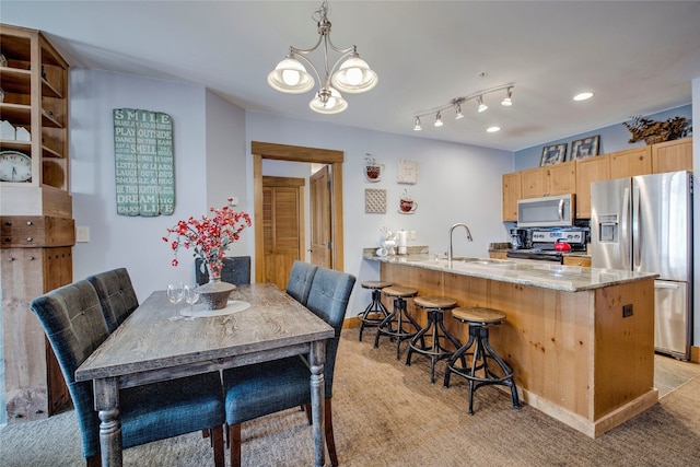 kitchen featuring a kitchen breakfast bar, light brown cabinetry, a sink, a chandelier, and appliances with stainless steel finishes
