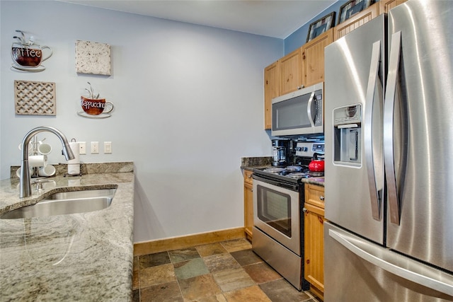 kitchen featuring stainless steel appliances, a sink, baseboards, stone finish floor, and light stone countertops