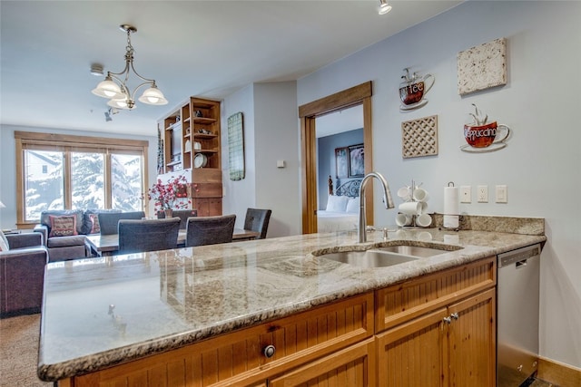 kitchen featuring light stone countertops, pendant lighting, stainless steel dishwasher, and a sink