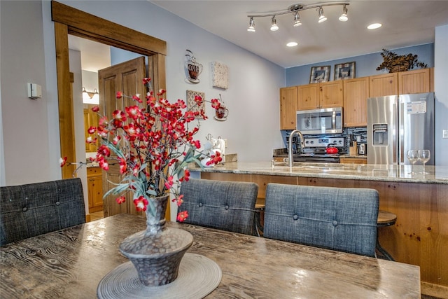 kitchen featuring a sink, light stone countertops, decorative backsplash, a peninsula, and appliances with stainless steel finishes