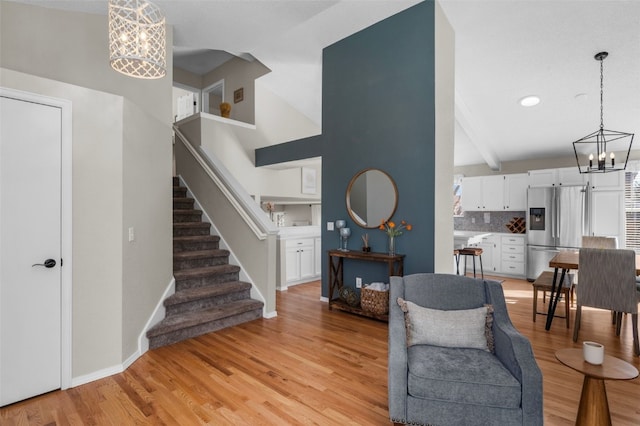 living area with baseboards, stairway, light wood finished floors, and an inviting chandelier