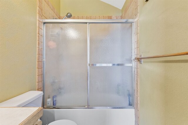 full bathroom featuring toilet, vanity, vaulted ceiling, and combined bath / shower with glass door