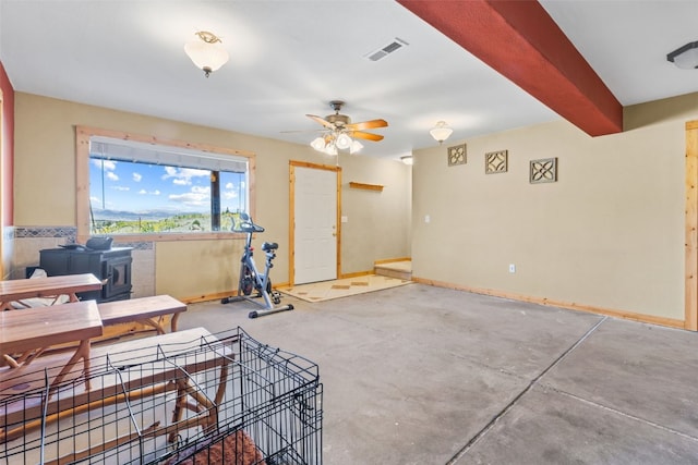 interior space featuring ceiling fan, beam ceiling, a wood stove, and concrete floors