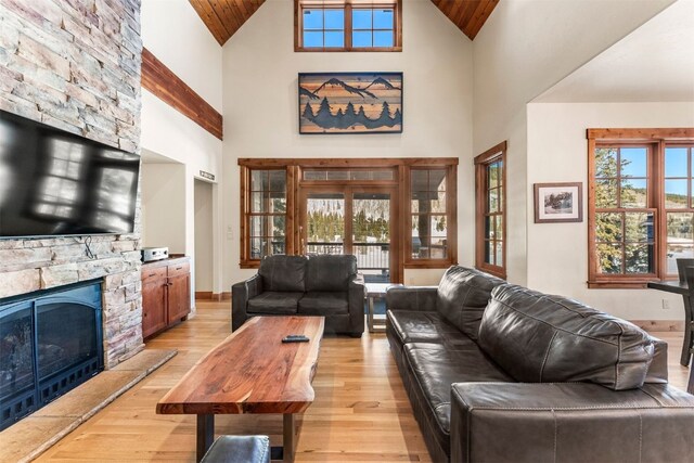 living area with high vaulted ceiling, light wood-type flooring, a fireplace, and baseboards