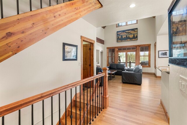 hallway with a towering ceiling, light wood finished floors, baseboards, and an upstairs landing