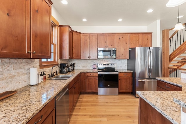 kitchen with appliances with stainless steel finishes, brown cabinets, a sink, and light stone countertops