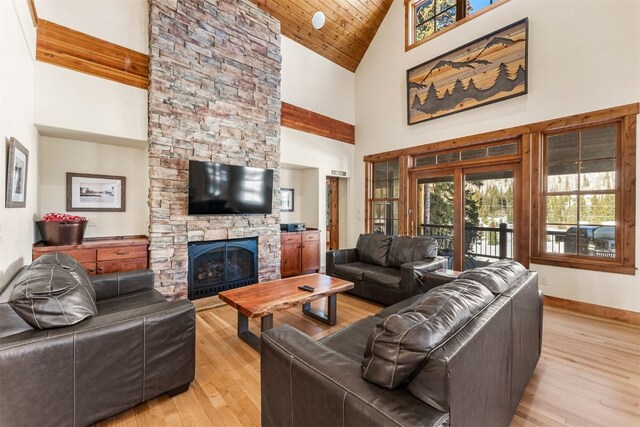 living area with baseboards, wood ceiling, light wood-style flooring, a stone fireplace, and high vaulted ceiling