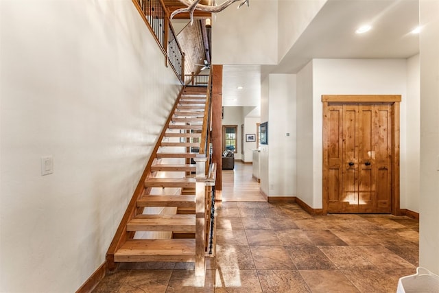 entrance foyer featuring stairs, stone finish flooring, a towering ceiling, and baseboards