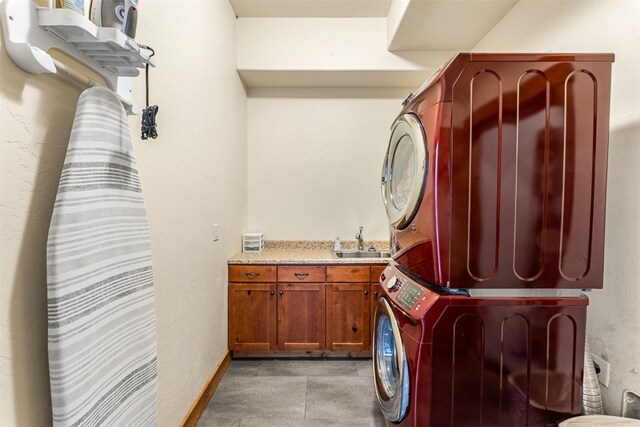 laundry area featuring a sink, stacked washer and dryer, baseboards, and cabinet space