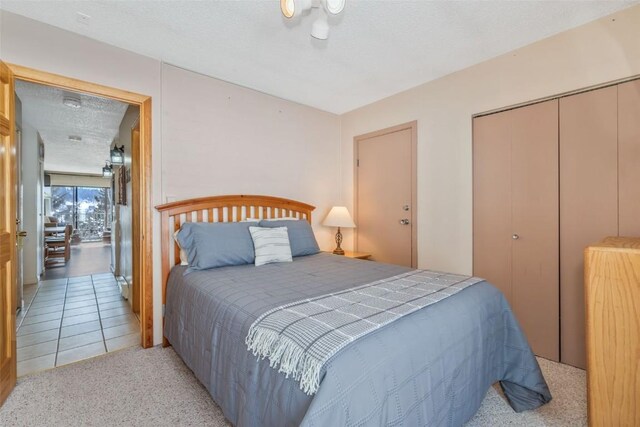 bedroom with a closet, light carpet, a textured ceiling, and light tile patterned floors