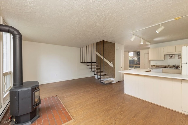 living room with a wood stove, rail lighting, a textured ceiling, and hardwood / wood-style flooring