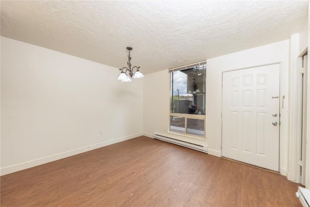 empty room with a textured ceiling, hardwood / wood-style flooring, baseboard heating, and a notable chandelier