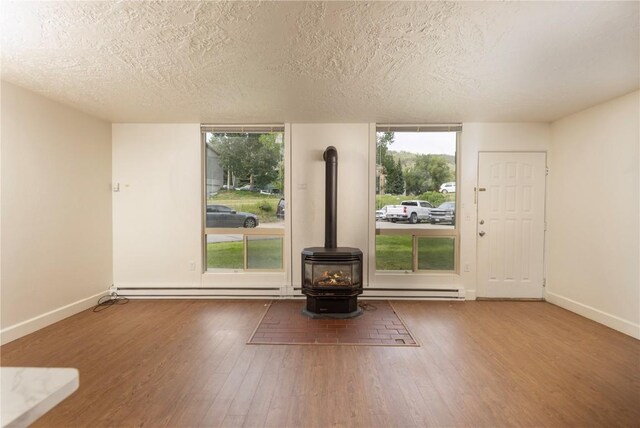 empty room with baseboard heating, a wood stove, wood-type flooring, and a textured ceiling