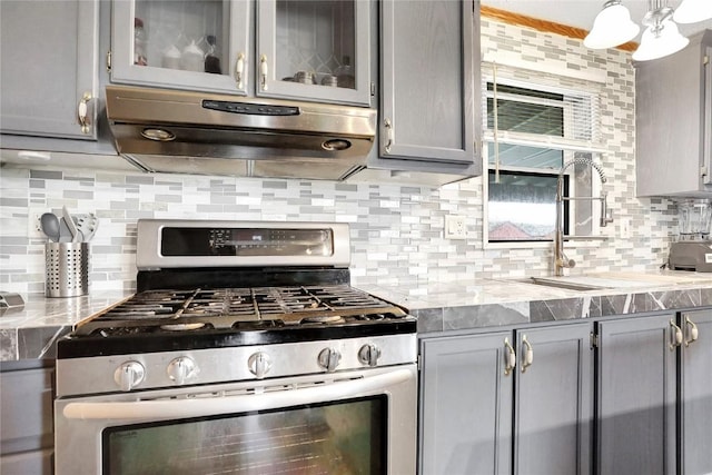 kitchen featuring tasteful backsplash, gray cabinetry, light stone countertops, and stainless steel range with gas stovetop