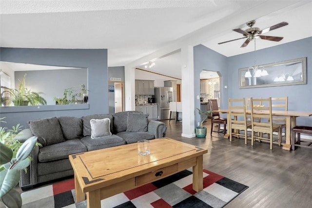 living room with ceiling fan with notable chandelier, dark hardwood / wood-style flooring, and vaulted ceiling