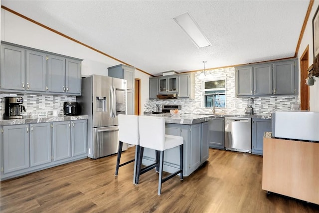 kitchen with appliances with stainless steel finishes, a kitchen breakfast bar, pendant lighting, gray cabinets, and a kitchen island