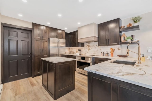 kitchen featuring high quality fridge, wall oven, a sink, custom exhaust hood, and open shelves