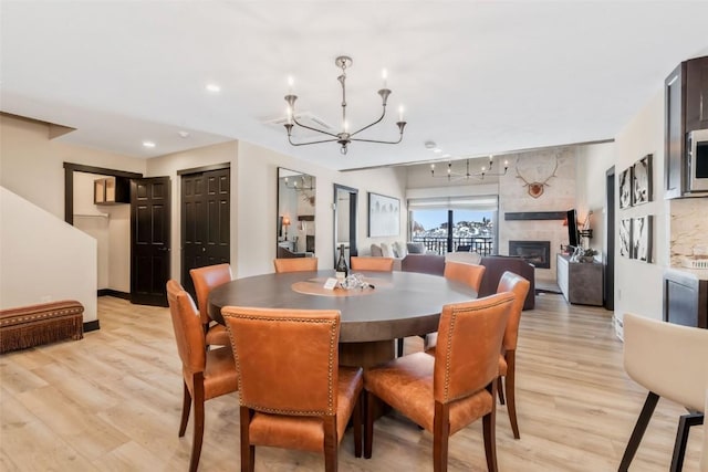 dining area with light wood finished floors, baseboards, a tiled fireplace, an inviting chandelier, and recessed lighting