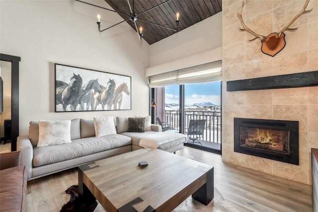 living room with high vaulted ceiling, wooden ceiling, a tiled fireplace, and wood finished floors