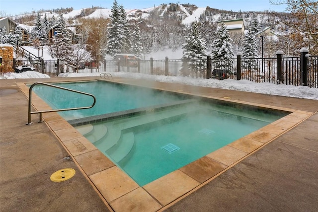 snow covered pool featuring a patio, fence, and an in ground hot tub