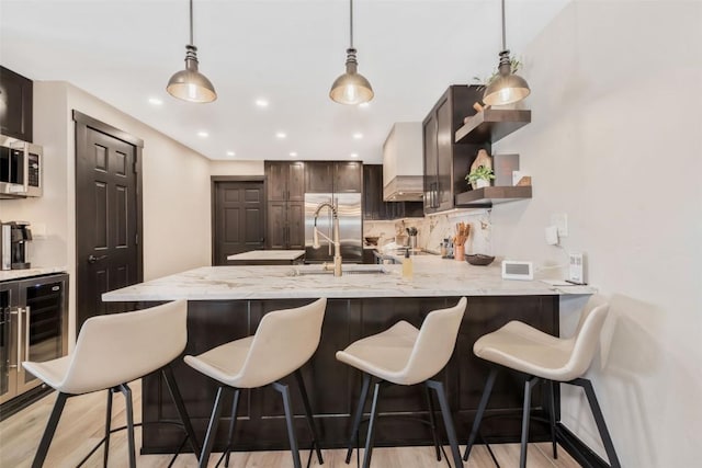 kitchen with light wood finished floors, decorative backsplash, dark brown cabinetry, a sink, and a peninsula