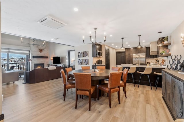 dining room featuring a tile fireplace, recessed lighting, light wood finished floors, and an inviting chandelier