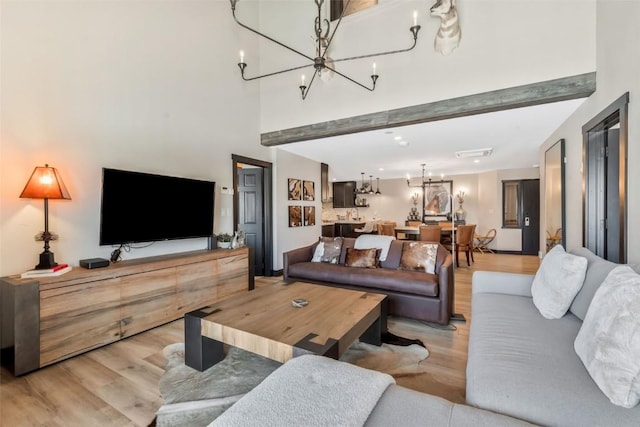 living area featuring light wood-style floors, a high ceiling, and a notable chandelier