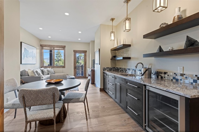 kitchen with sink, beverage cooler, light stone counters, light hardwood / wood-style floors, and decorative light fixtures