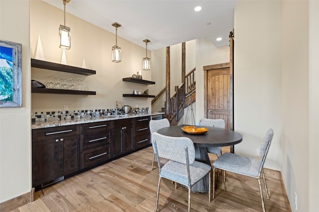 kitchen with backsplash, dark brown cabinetry, sink, decorative light fixtures, and light hardwood / wood-style flooring