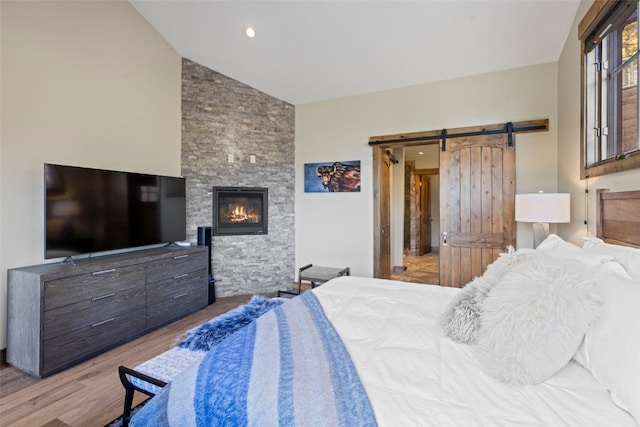 bedroom featuring hardwood / wood-style flooring, a barn door, a stone fireplace, and vaulted ceiling