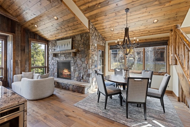 dining room with wooden ceiling, a chandelier, vaulted ceiling with beams, light hardwood / wood-style floors, and a stone fireplace