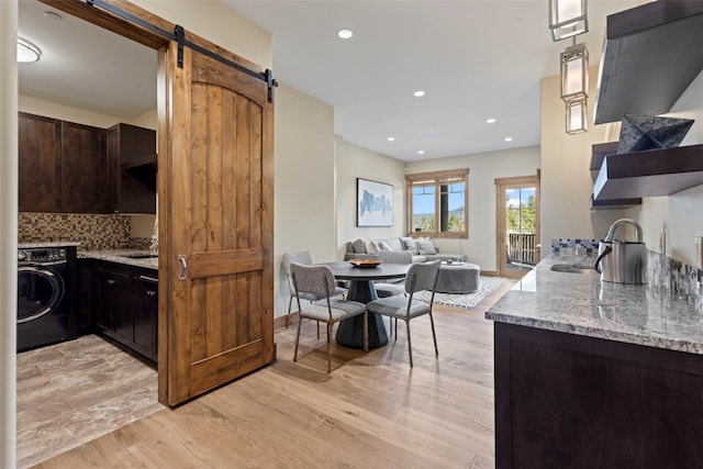 kitchen with backsplash, light stone counters, a barn door, light hardwood / wood-style flooring, and washer / dryer