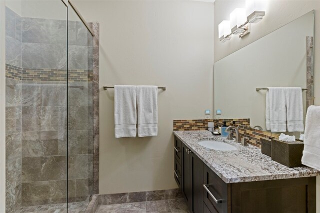 bathroom with vanity, a tile shower, and backsplash