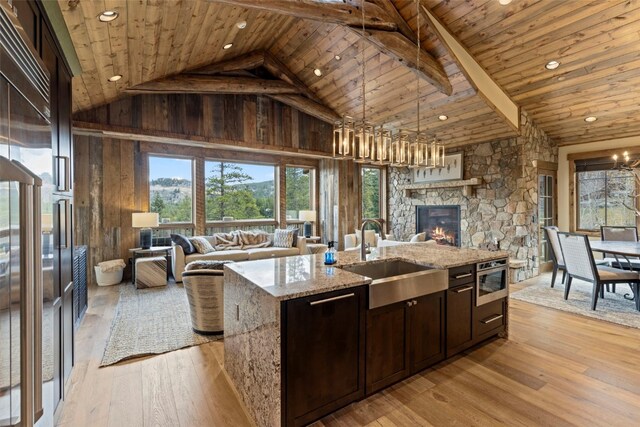 kitchen featuring light stone countertops, a kitchen island with sink, sink, light hardwood / wood-style flooring, and a fireplace