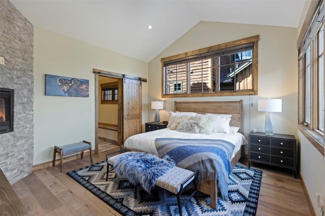 bedroom featuring a barn door, a stone fireplace, wood-type flooring, and lofted ceiling