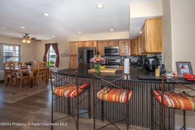 kitchen with kitchen peninsula, a kitchen breakfast bar, stainless steel appliances, ceiling fan, and dark hardwood / wood-style floors