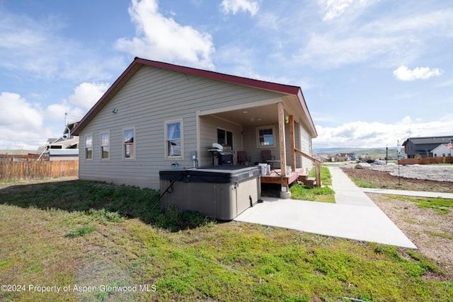 back of property with a lawn and a hot tub