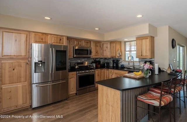 kitchen featuring kitchen peninsula, appliances with stainless steel finishes, a breakfast bar, dark wood-type flooring, and sink