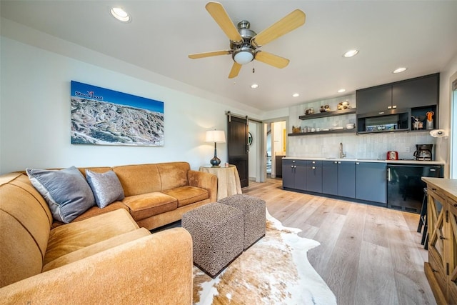 living room with ceiling fan, a barn door, indoor wet bar, and light hardwood / wood-style floors