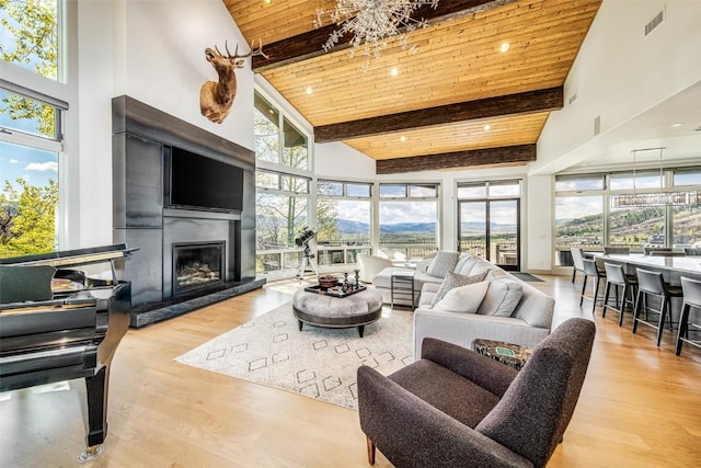 living room with a high ceiling, a fireplace, beamed ceiling, light hardwood / wood-style floors, and wood ceiling