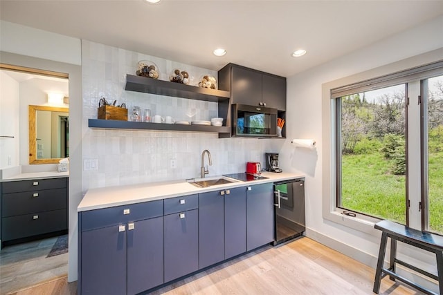 kitchen with blue cabinets, sink, black dishwasher, tasteful backsplash, and light hardwood / wood-style floors