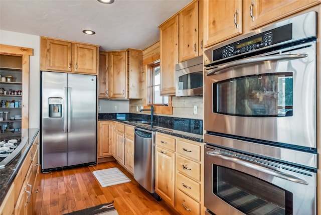 kitchen with light wood-type flooring, a sink, stainless steel appliances, dark stone counters, and decorative backsplash