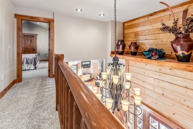 corridor with wooden walls, carpet floors, recessed lighting, a notable chandelier, and an upstairs landing