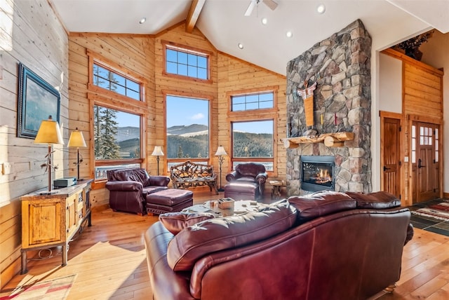 living area with wooden walls, high vaulted ceiling, beam ceiling, a fireplace, and light wood-style floors