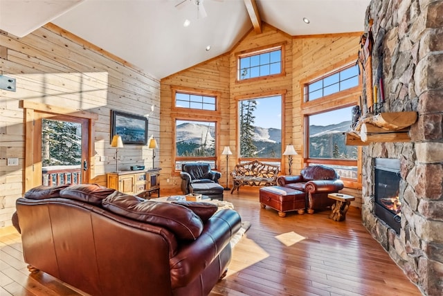 living room featuring beamed ceiling, high vaulted ceiling, a stone fireplace, and wood walls