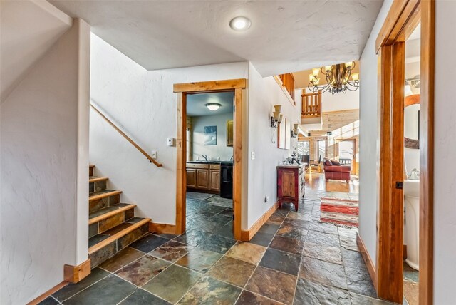 foyer entrance featuring stone tile flooring, stairway, baseboards, and a notable chandelier