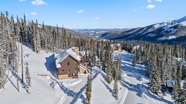 snowy aerial view with a wooded view and a mountain view