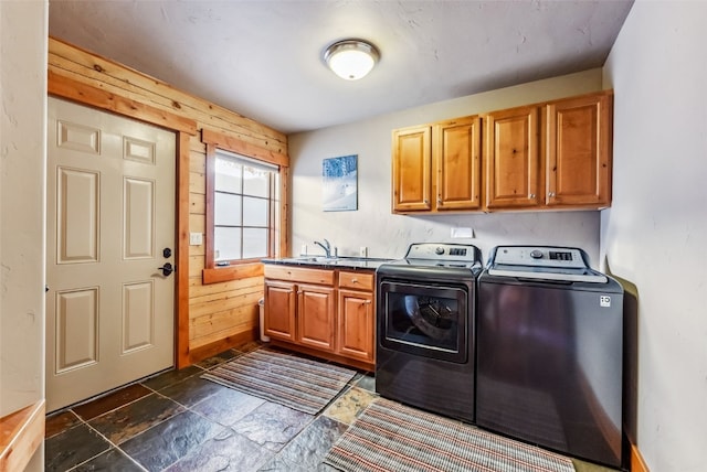 washroom featuring washer and clothes dryer, wood walls, stone tile floors, cabinet space, and a sink