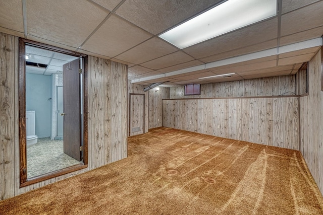 basement with a paneled ceiling, carpet, and wooden walls